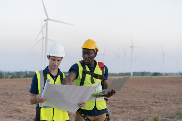 Two male construction workers in a field with wind turbines